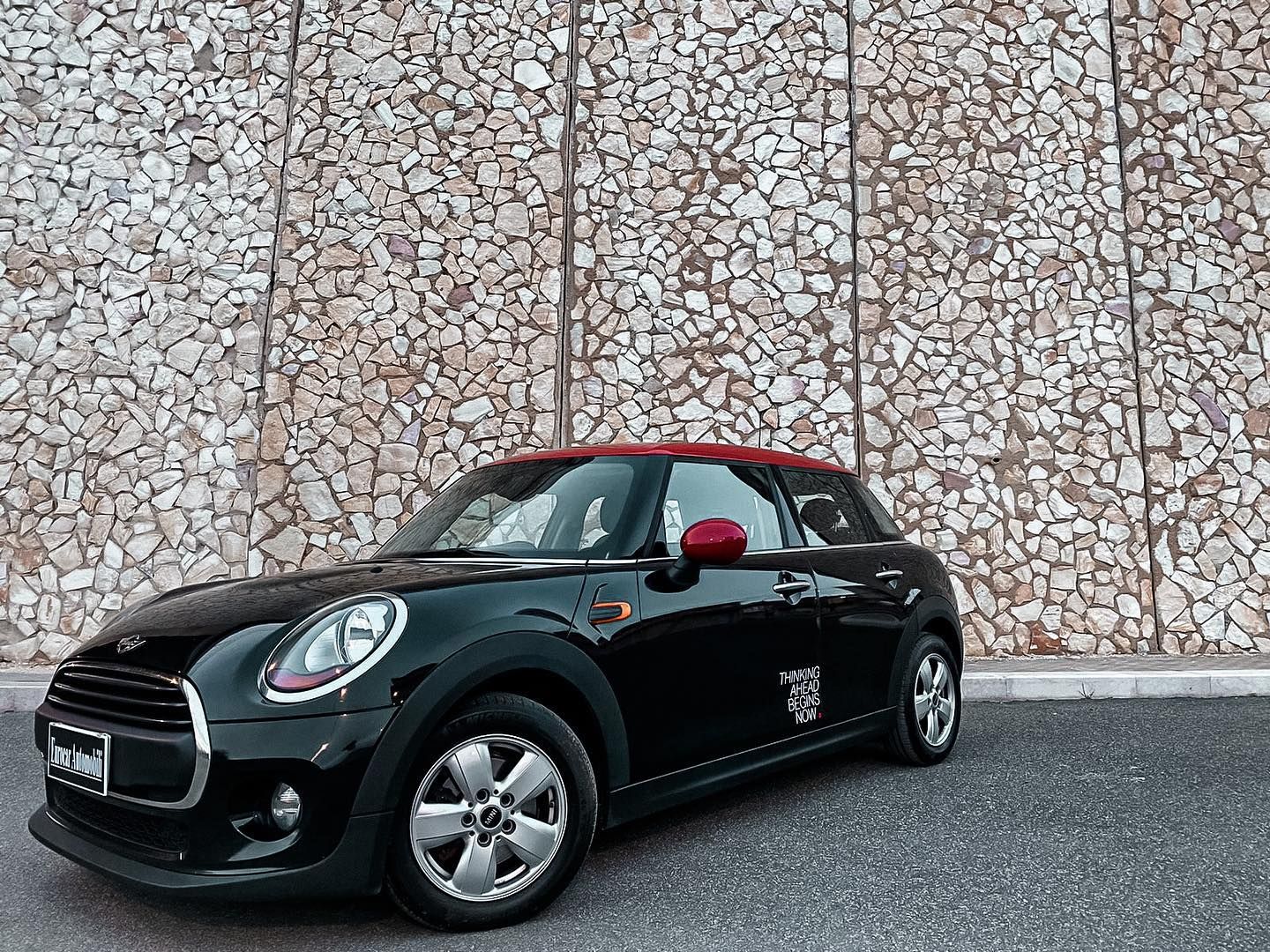 una mini cooper nera è parcheggiata davanti a un muro di pietra.