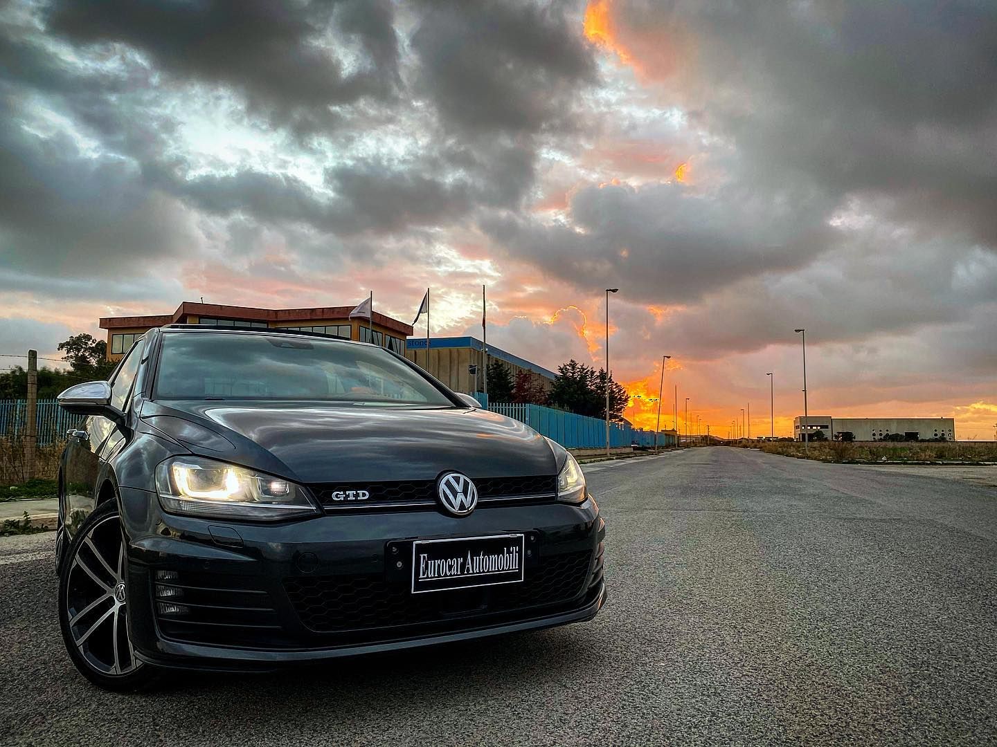 una Volkswagen Golf nera è parcheggiata sul lato della strada al tramonto.