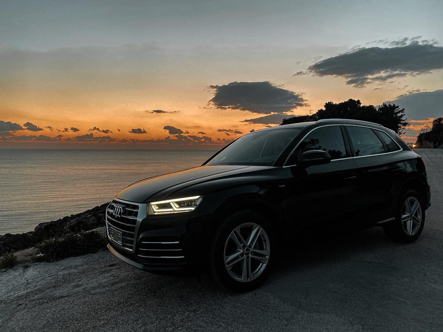 un'auto nera è parcheggiata sul lato di una strada vicino all'oceano al tramonto.