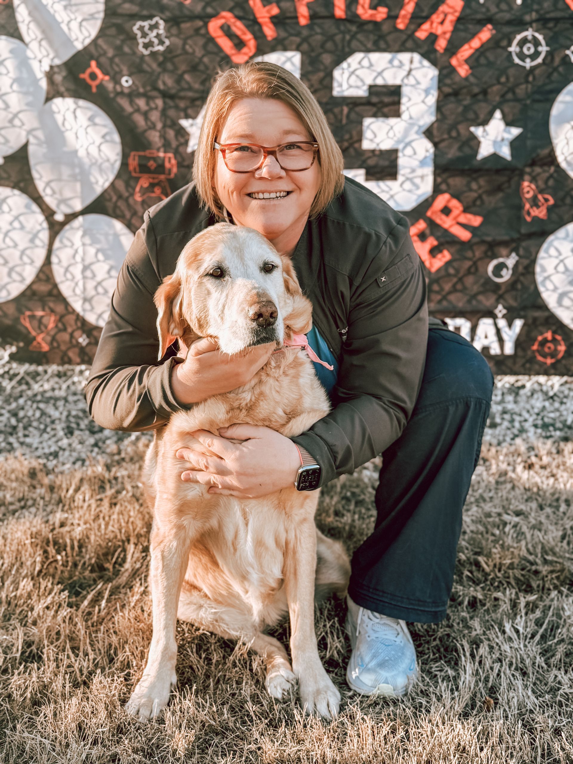 Lacie is kneeling down next to a dog in front of a banner.