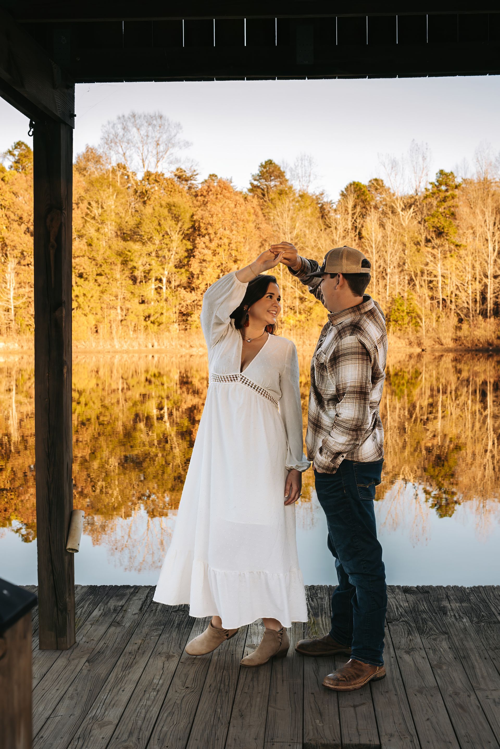 A man and a woman are dancing on a dock next to a lake.