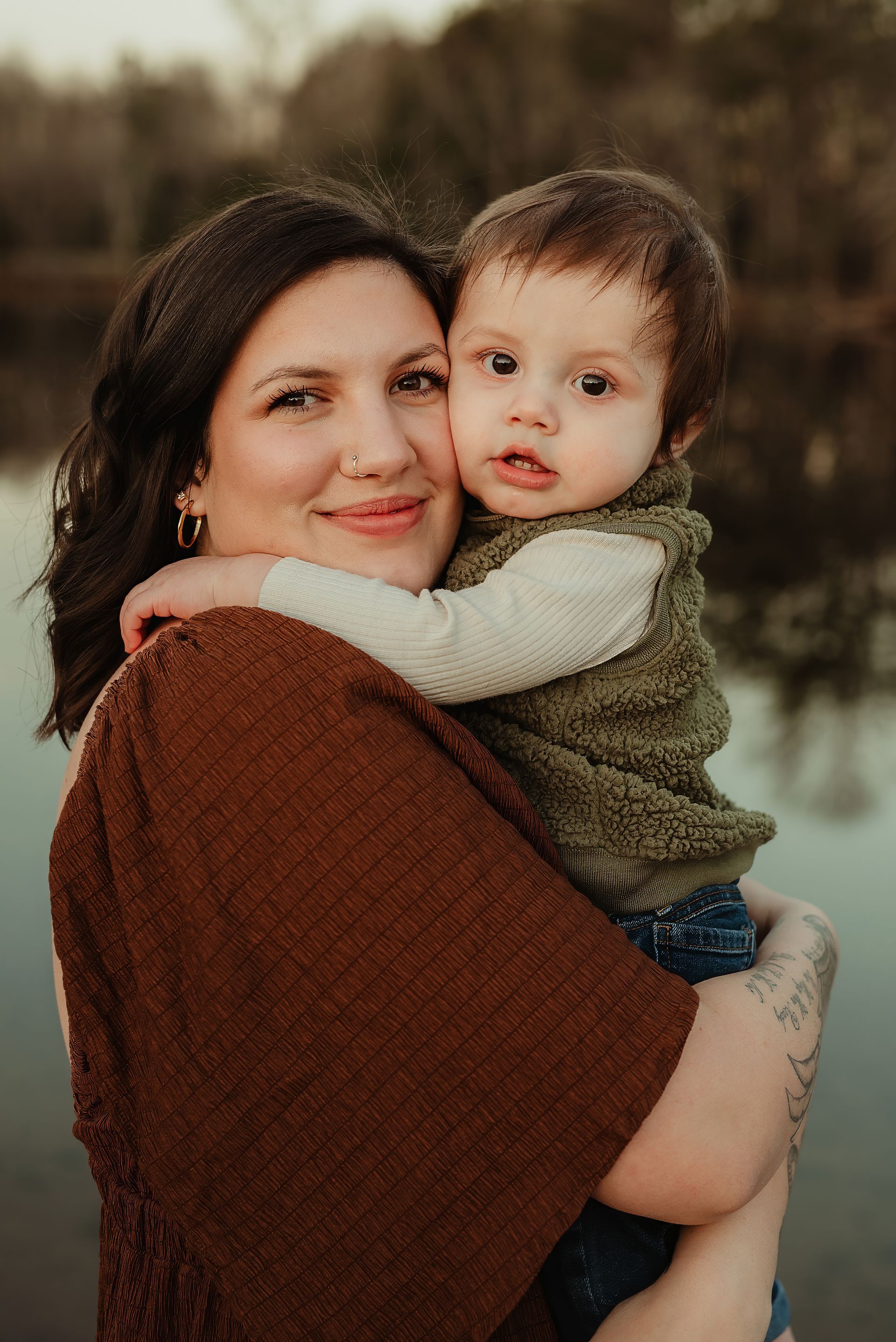 Raelynn is holding a baby in her arms in front of a body of water.