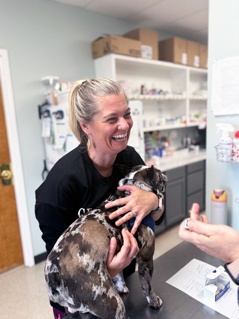 Bonnie is holding a dog on a table in a veterinary office.