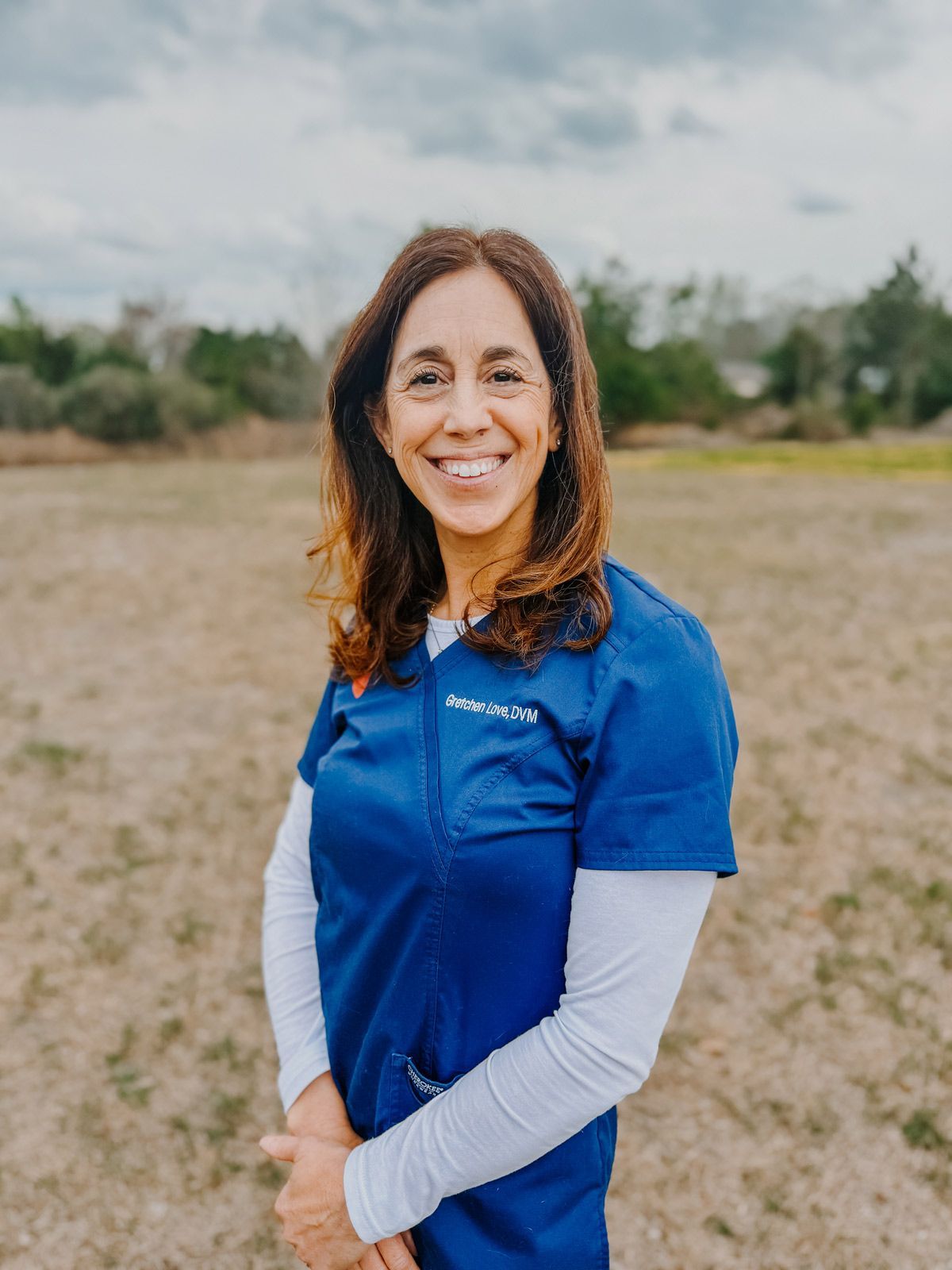 A woman in a blue scrub is smiling in a field.
