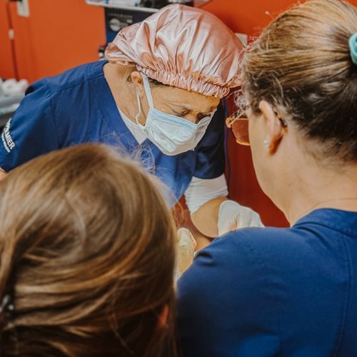 A surgeon wearing a mask and a pink hat is talking to two women.