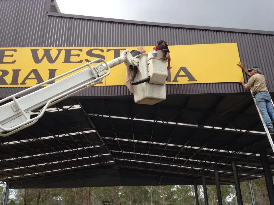 A man in a bucket is hanging a sign on the side of a building