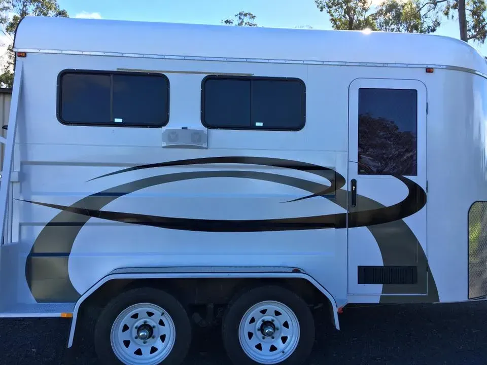 A white horse trailer is parked on the side of the road.