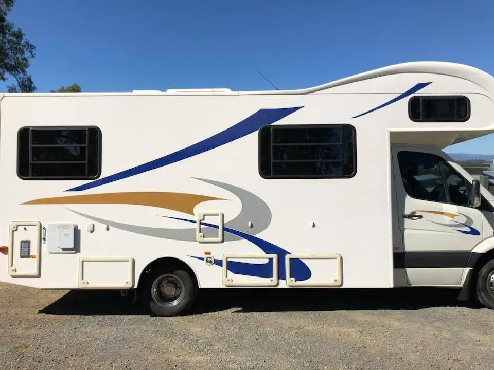 A white and blue rv is parked in a gravel lot.