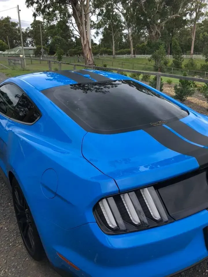 A blue mustang with black stripes is parked on the side of the road.