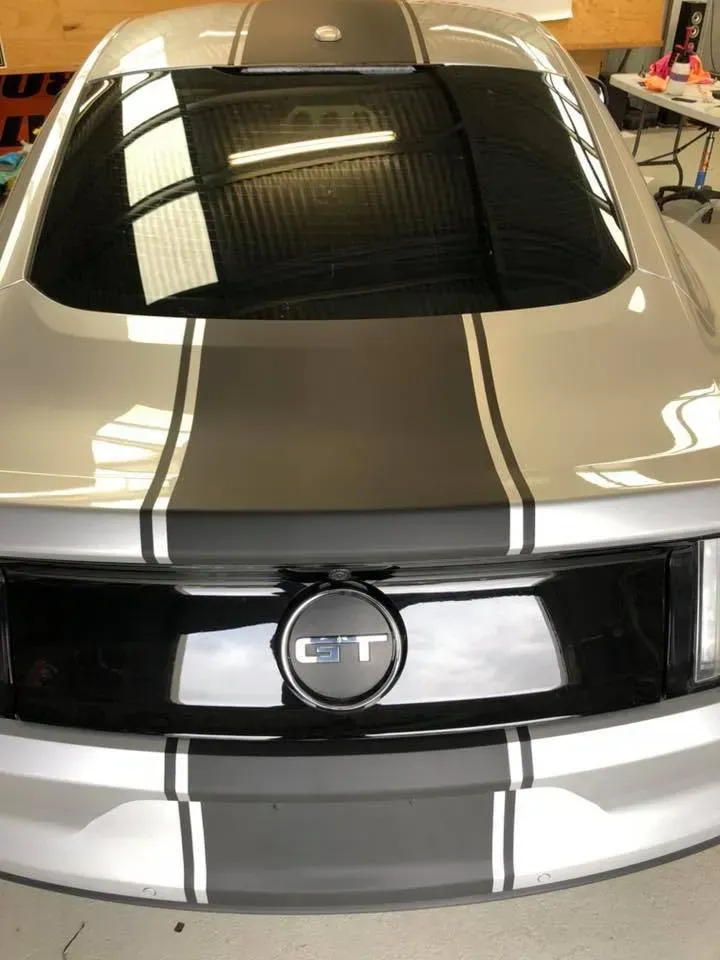 A silver mustang with black and white stripes is parked in a garage.