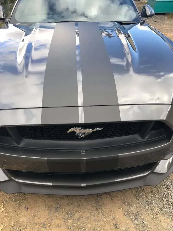 The front of a gray mustang with black stripes on the hood.