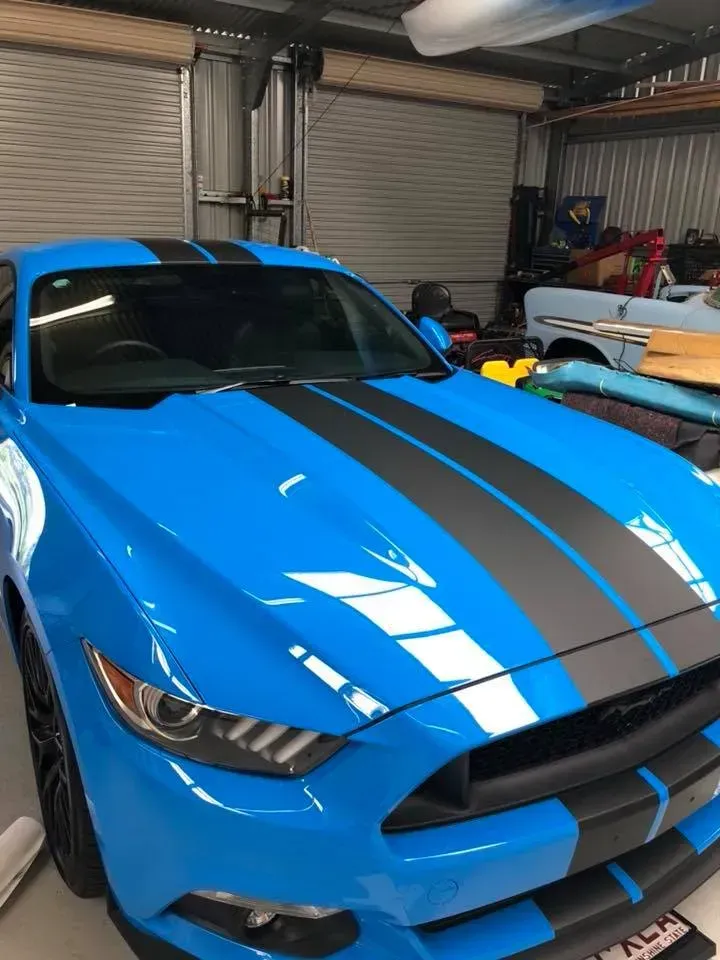 A blue mustang with black stripes is parked in a garage.