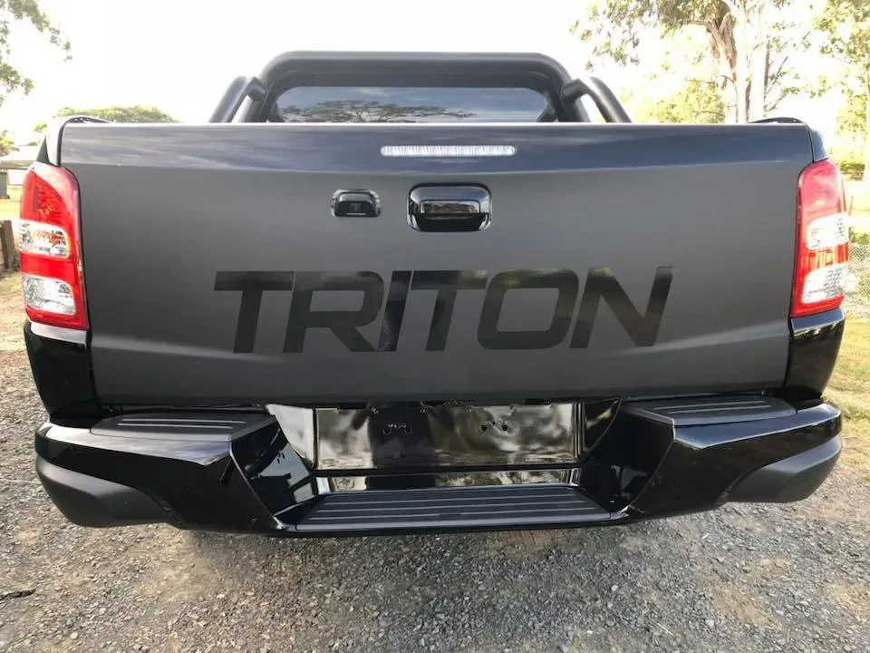 A black triton truck is parked on a gravel road.