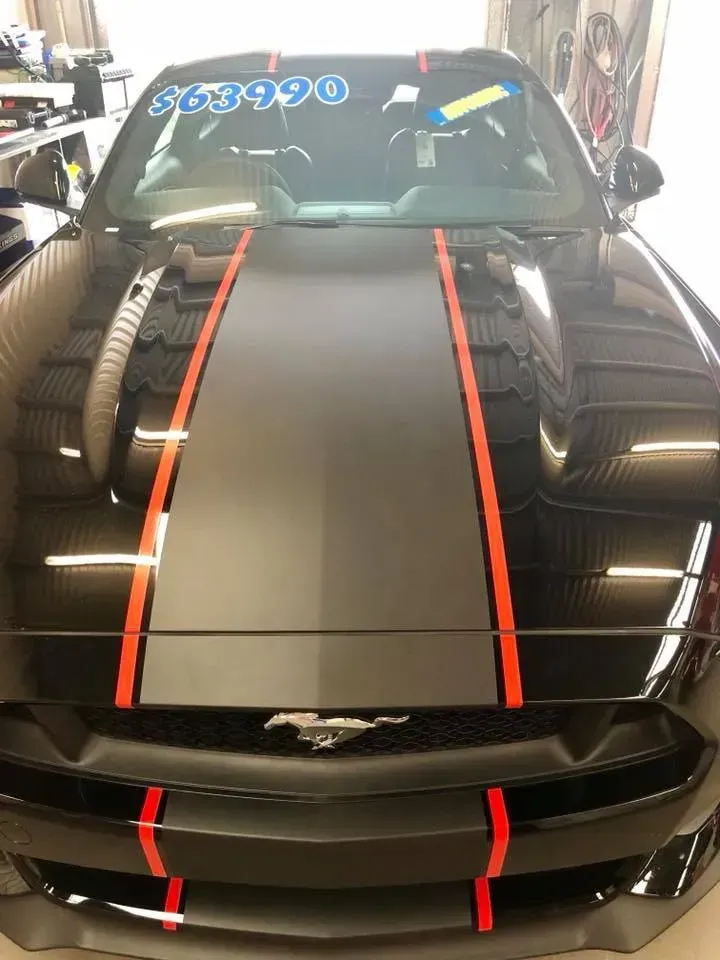 A black mustang with red stripes on the hood is parked in a garage.