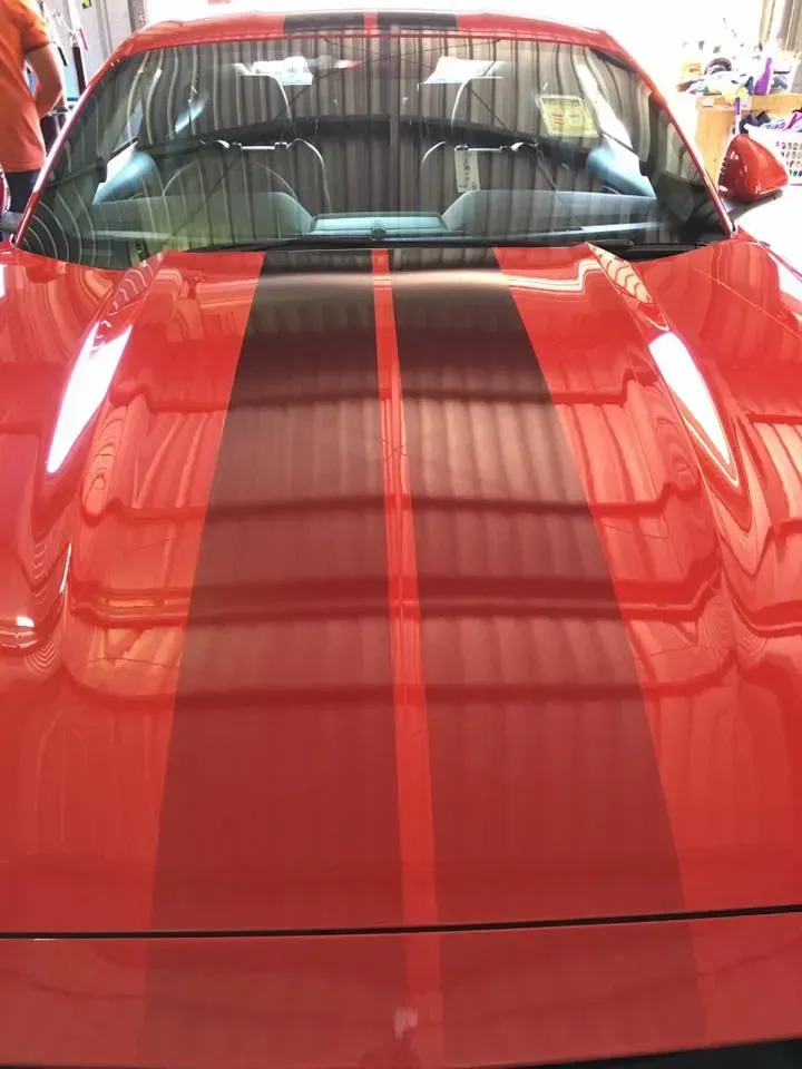 A red sports car with black stripes on the hood is parked in a garage.