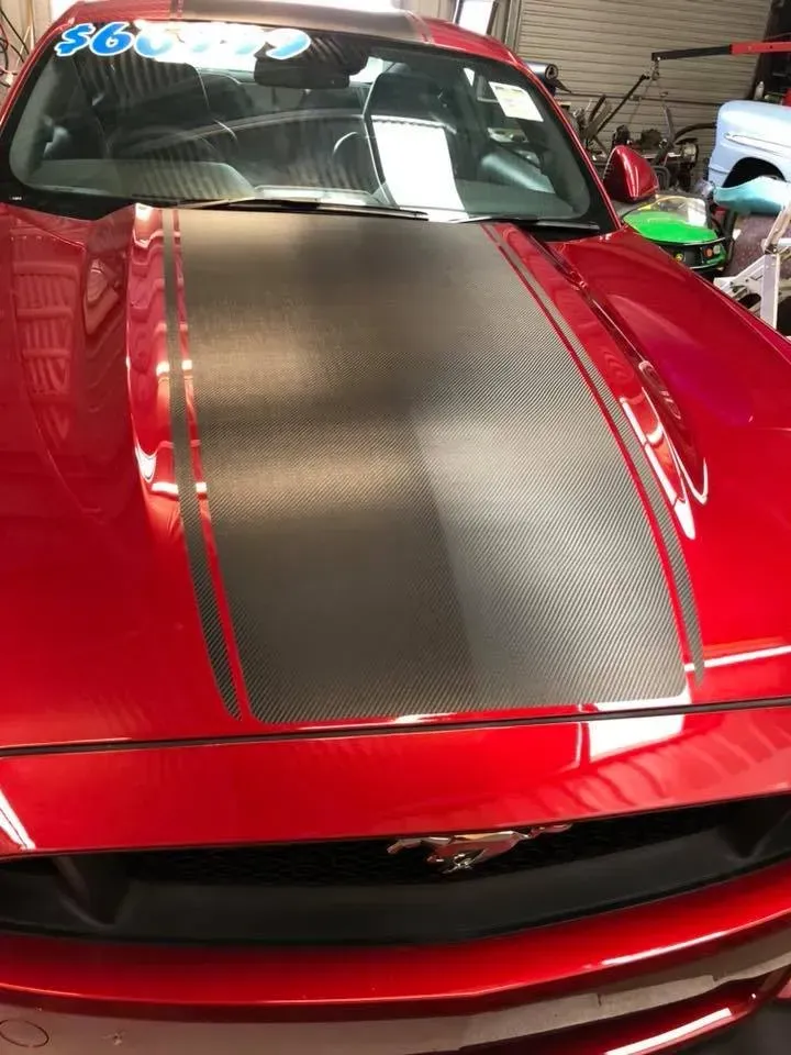 A red mustang with a black hood stripe is parked in a garage.
