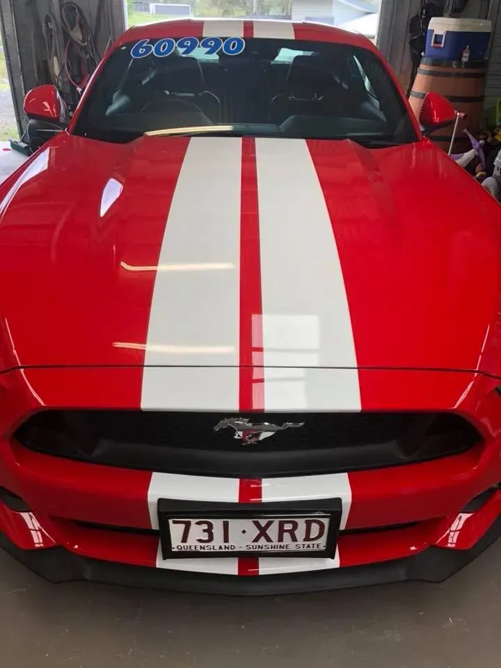 A red mustang with white stripes on the hood is parked in a garage.