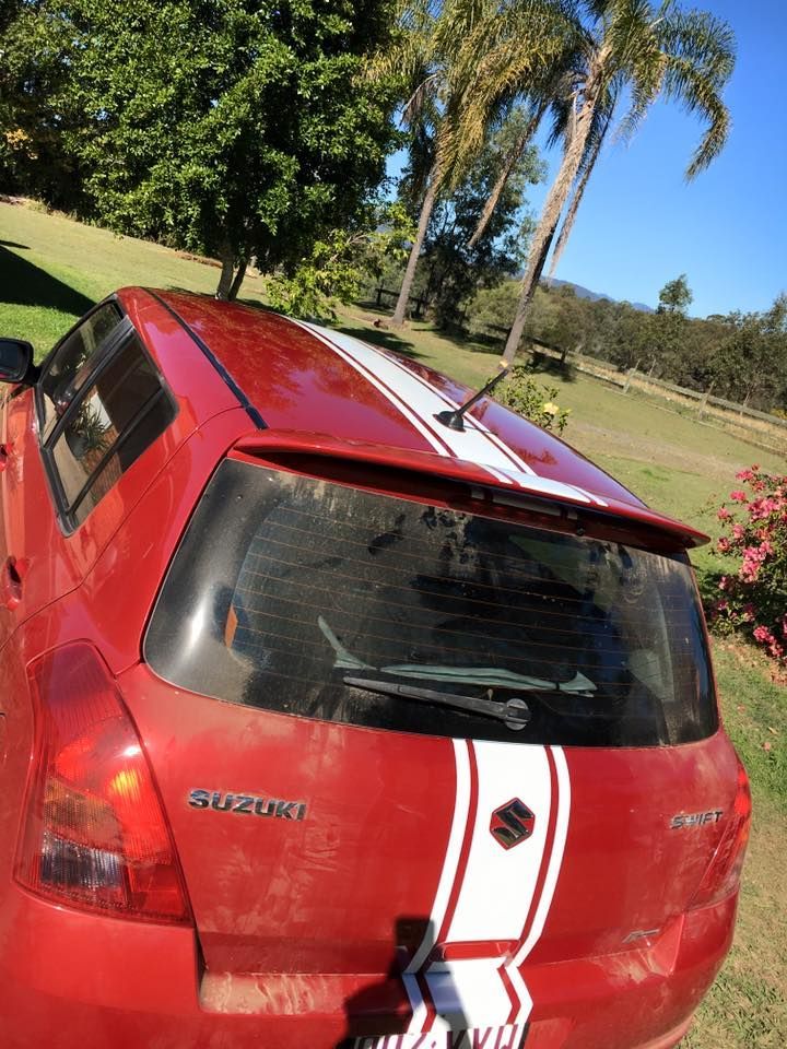 A red suzuki car is parked in a grassy field.