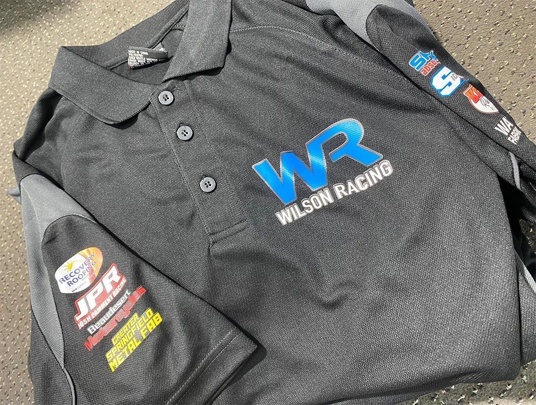 A black wilson racing polo shirt is laying on the ground.