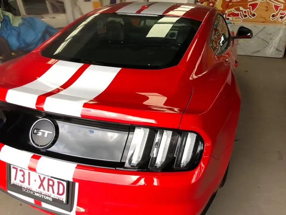 A red mustang with white stripes on the roof is parked in a garage.