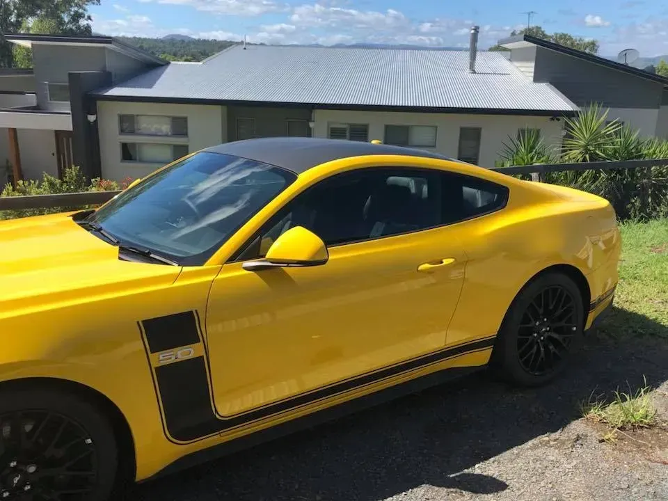 A yellow mustang is parked in front of a house.