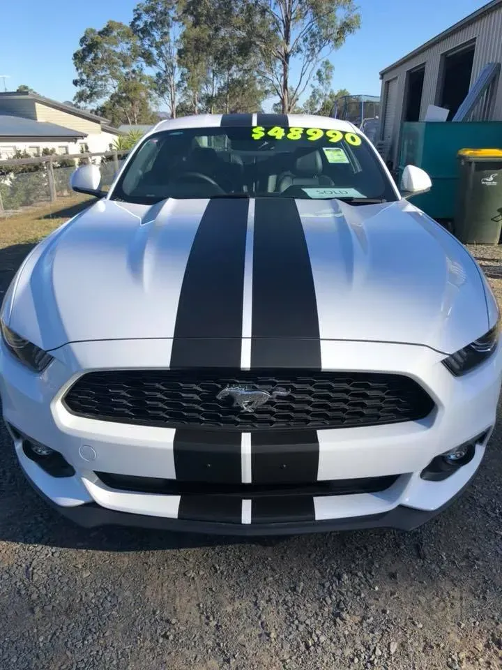 A white mustang with black stripes is parked on a gravel road.