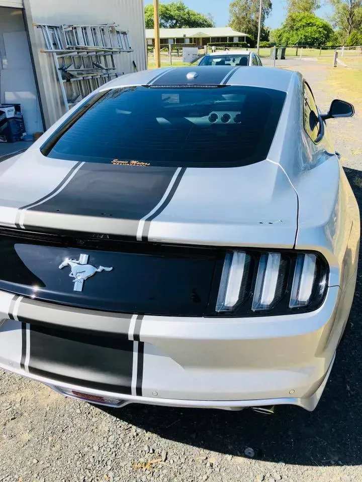 A silver mustang with black stripes is parked in a parking lot.