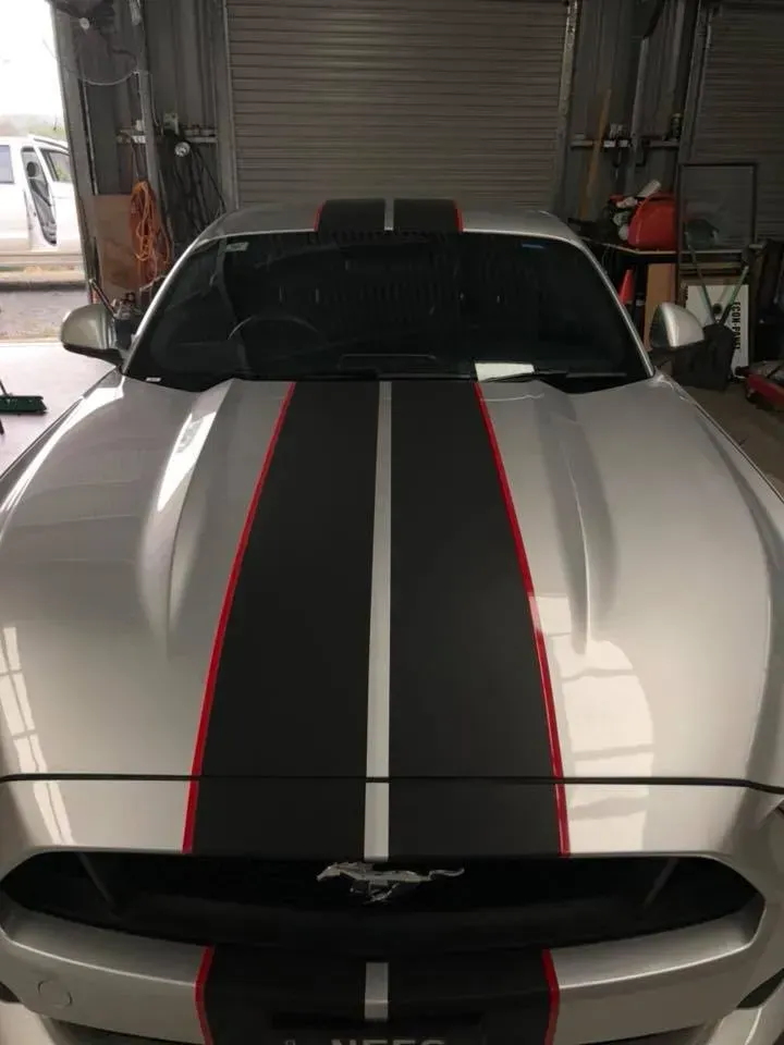 A silver mustang with black and red stripes on the hood is parked in a garage.