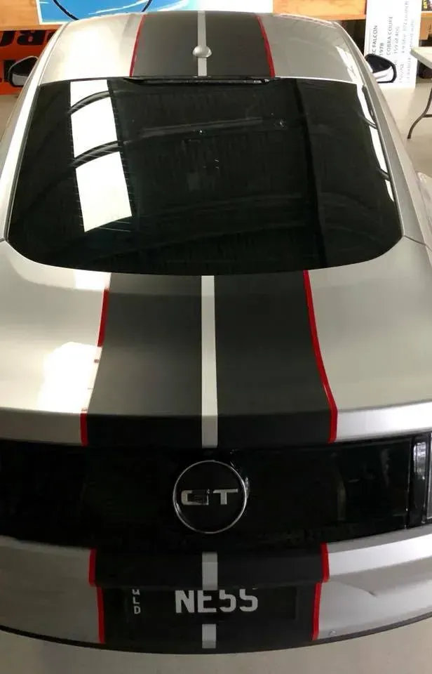 The back of a silver mustang with black and red stripes on the hood.