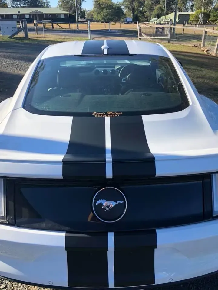 A white mustang with black stripes on the hood is parked in a parking lot.