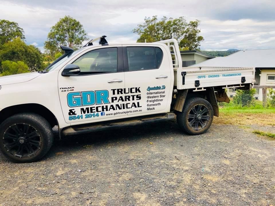 A white truck with a flat bed is parked in a gravel lot.