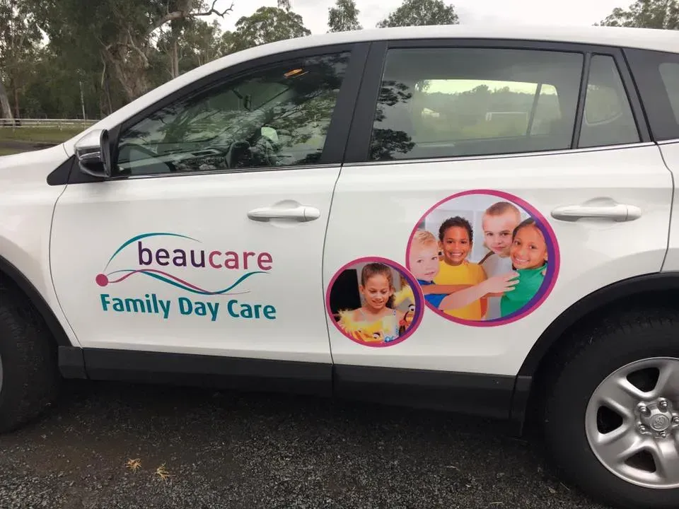 A white car with a sticker on the side that says beaucare family day care.