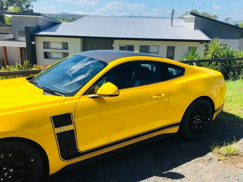 A yellow mustang is parked in front of a house