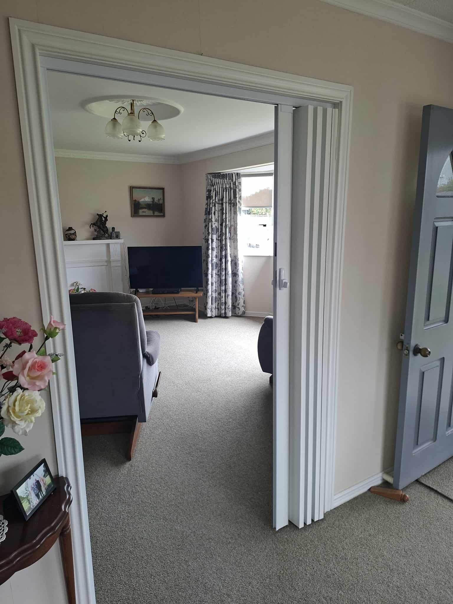 Living room interior viewed through a doorway with a decorative frame. Contains a TV, couch, and curtains.