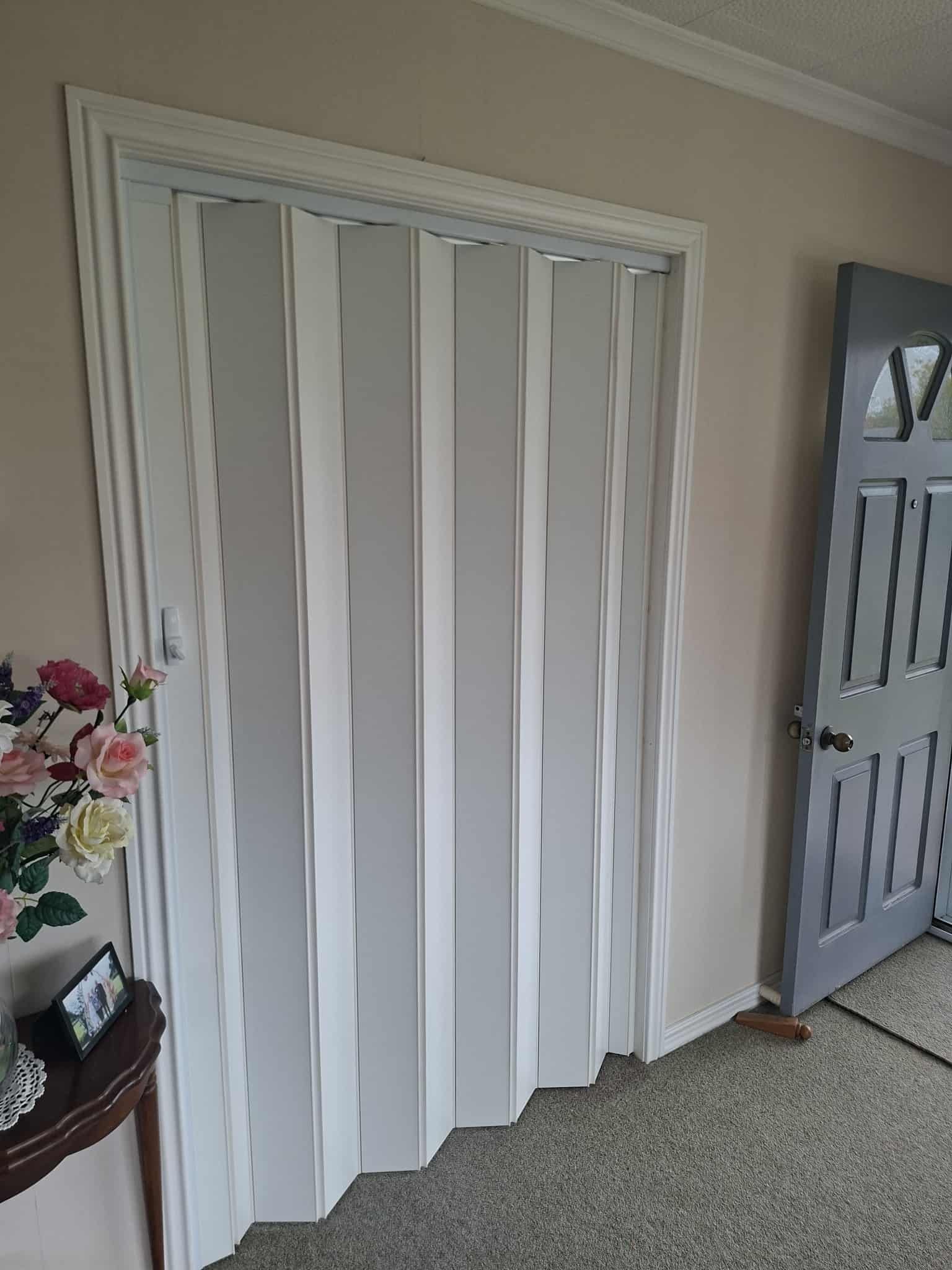 White accordion door in a doorway, next to a gray door.