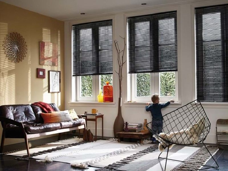 Living room with black blinds, child looking out window, and a dark brown sofa.