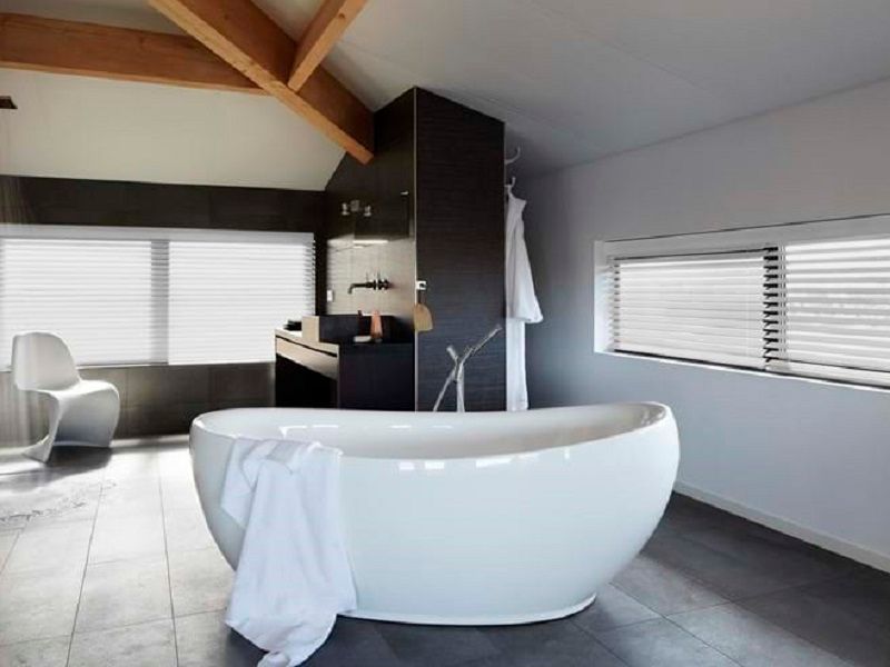 Modern bathroom with a white oval bathtub, blinds, and a white chair.