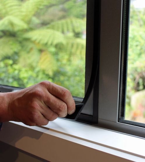 Person's hand pulling back a black screen from a window frame, revealing a green blurred background.