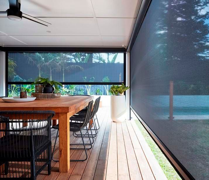 Outdoor patio with wooden table, chairs, and dark mesh roller shades.