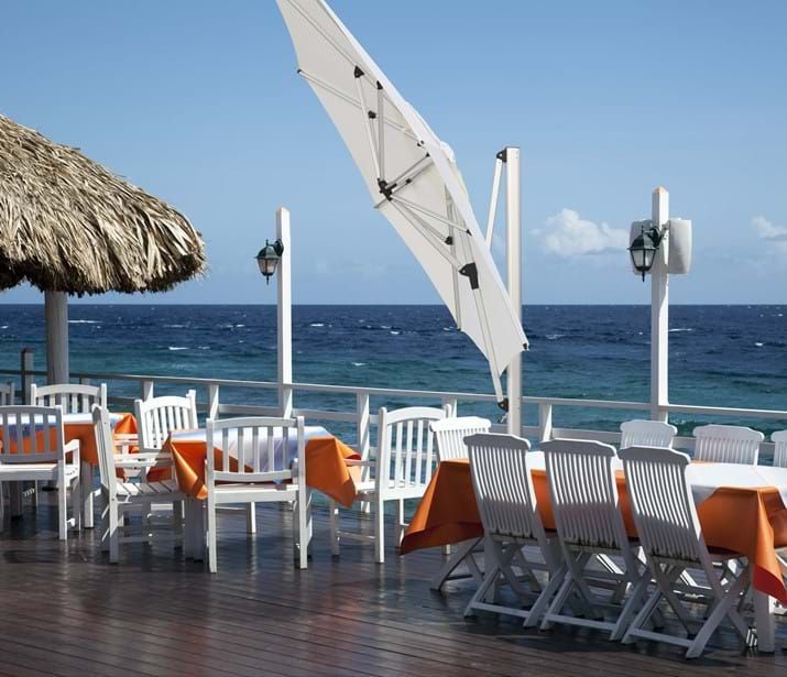 Outdoor restaurant with white tables, orange tablecloths, and a thatch roof, overlooking the blue ocean. Outdoor restaurant with white tables, orange tablecloths, and a thatch roof, overlooking the blue ocean.