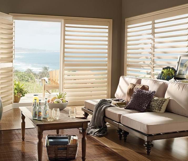 Living room with wooden shutters, a view of the ocean, a beige sofa, and a wooden coffee table.