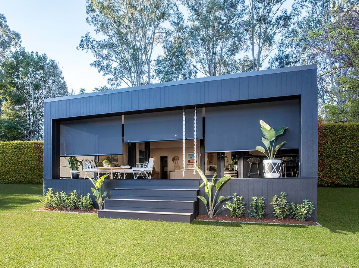 Gray pergola over a patio with white furniture, plants, and a light-colored building.