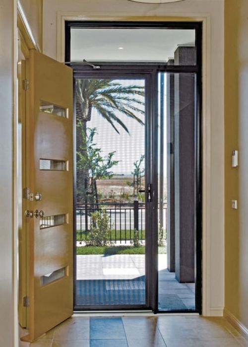 Open beige door with decorative cutouts, leading to a screen door with a view of a yard and palm tree.