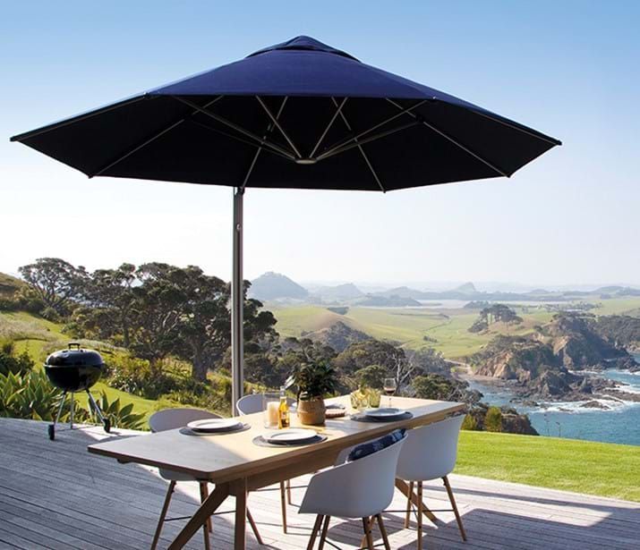 Blue patio umbrella over a table set for a meal on a deck overlooking a coastal landscape.