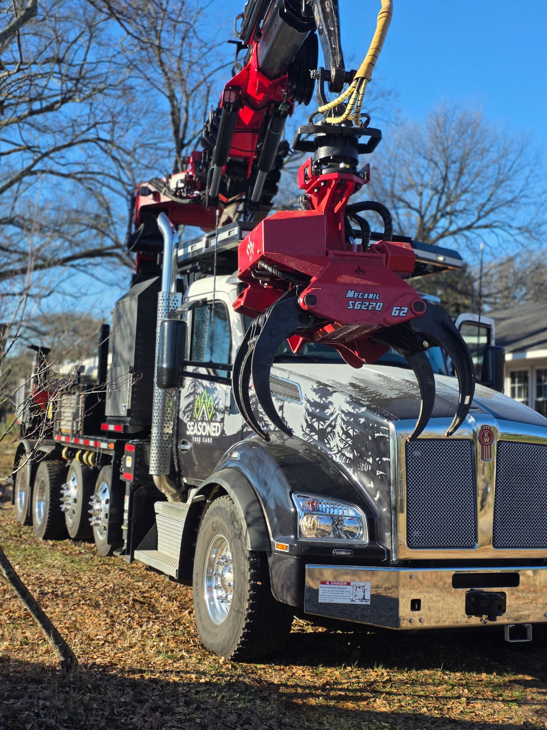 Red tow truck with crane arm lifting equipment on a sunny roadside with bare trees