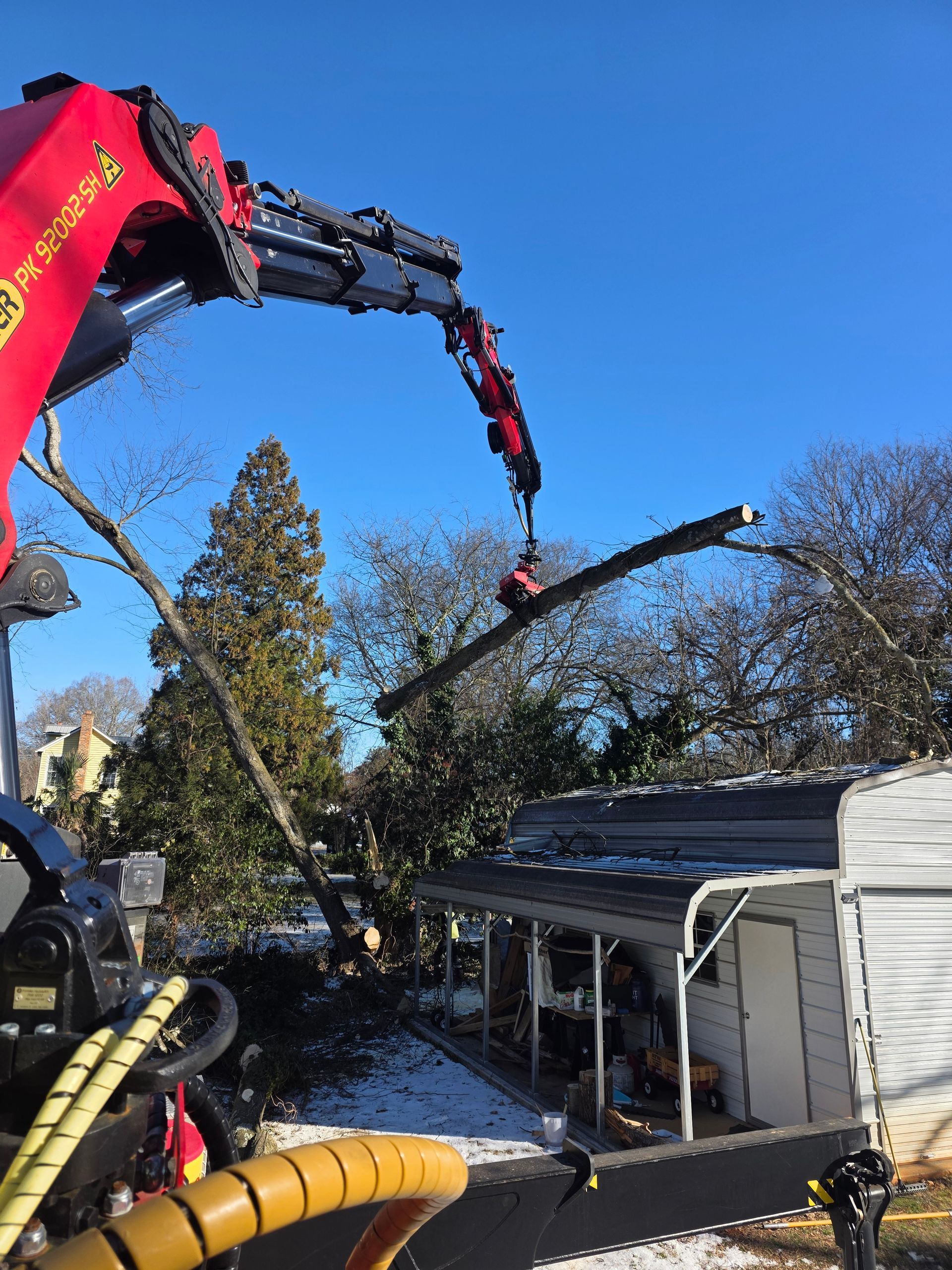 Crane lifting roof debris from a snowy house under a clear blue sky