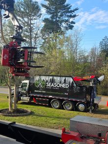 Red crane lifting a black “SEASONED” truck in a wooded outdoor setting