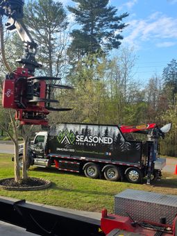 Red crane lifting a black “SEASONED” truck in a wooded outdoor setting