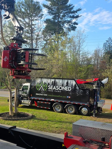 Red crane lifting a black “SEASONED” truck in a wooded outdoor setting