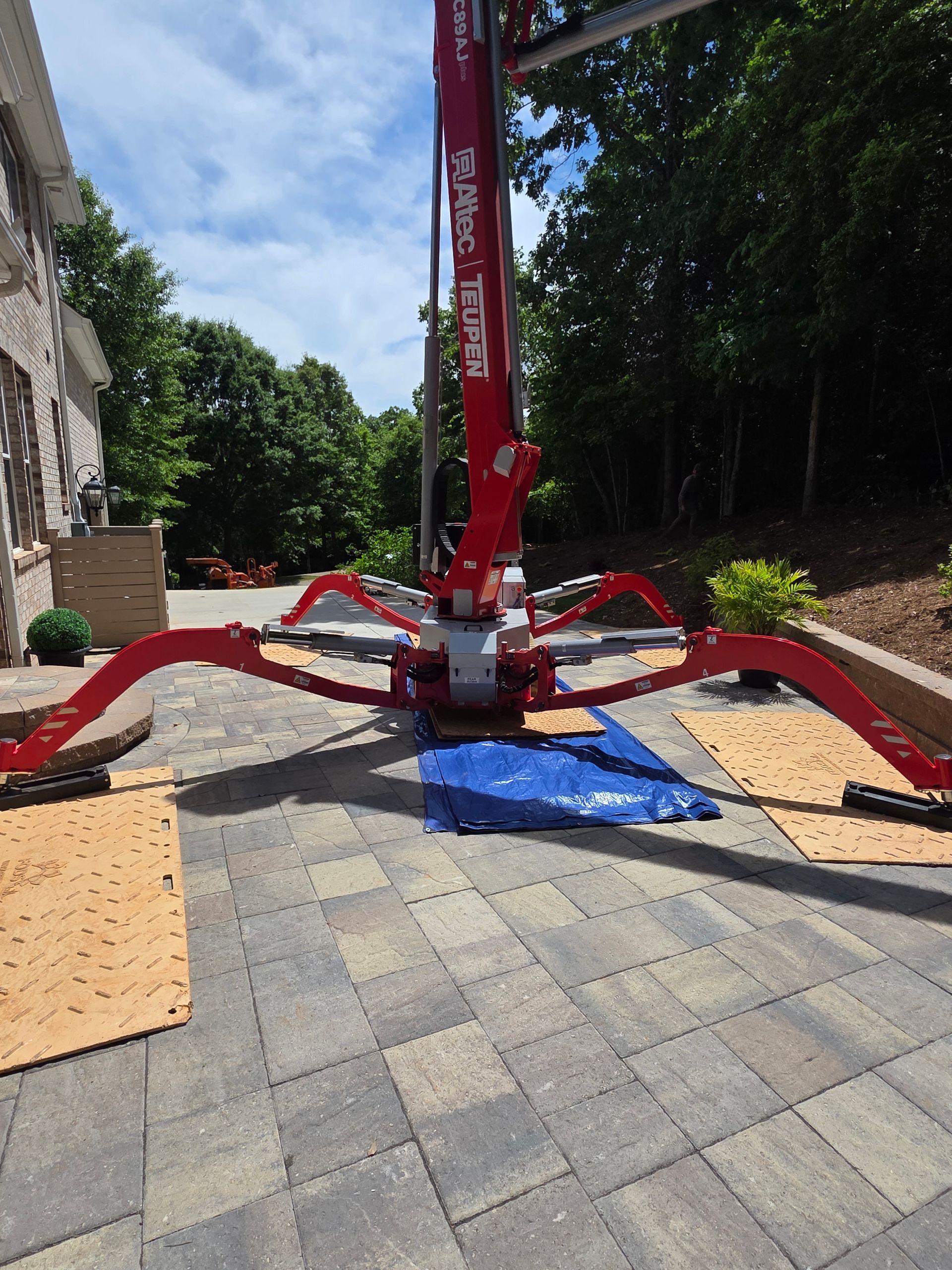Red construction vacuum lift with spread-out arms on a paved patio in bright sunlight